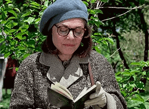 a woman wearing a beret and glasses is reading a book in the park .