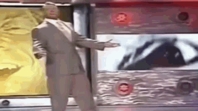 a man in a suit and tie is standing in front of a television screen .