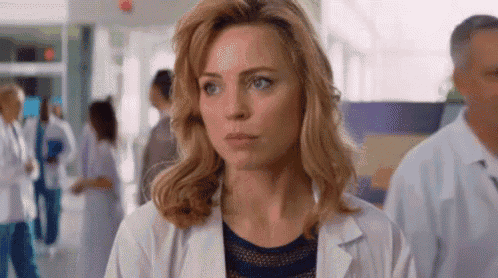 a woman in a white lab coat is standing in a hospital hallway with other doctors .