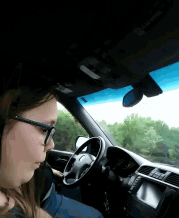 a woman wearing glasses is sitting in the driver 's seat of a vehicle