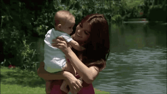 a woman is holding a baby in her arms in front of a body of water