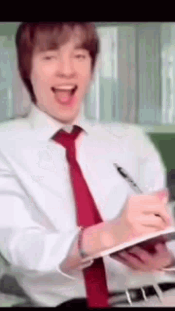 a man in a white shirt and red tie is laughing while holding a notebook .