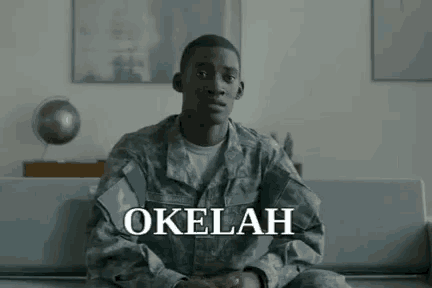 a man in a military uniform is sitting on a couch with the word okelah written above him .