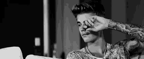 a black and white photo of justin bieber sitting on a couch with his hand on his face .
