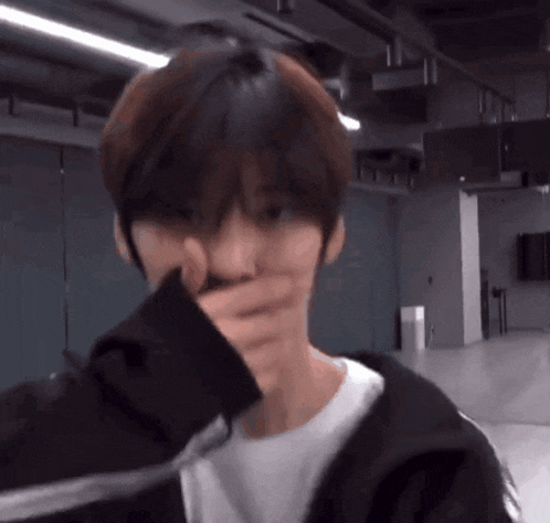 a young man is covering his mouth with his hand while standing in a room .