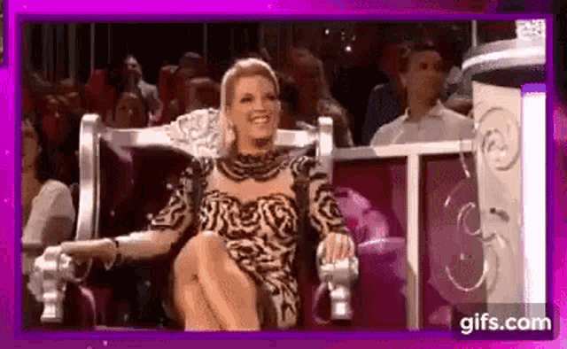 a woman in a leopard print dress is sitting in a chair with her legs crossed and smiling .
