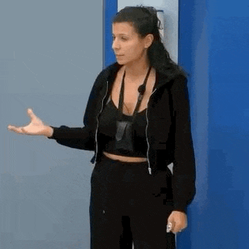 a woman in a black jacket and black pants is standing in front of a blue wall and making a funny face .