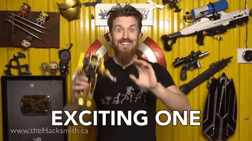 a man with a beard holds a toy in front of a yellow wall that says exciting one