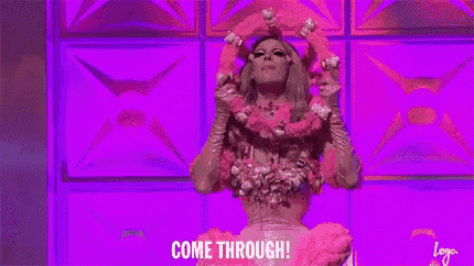 a drag queen in a pink dress is standing on a stage and holding a crown .
