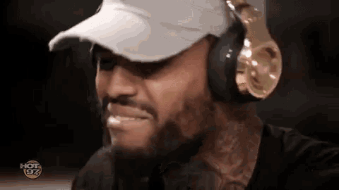a man wearing headphones and a hat is smiling and looking down .