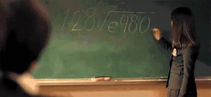 a woman is writing on a blackboard in a classroom with chalk .