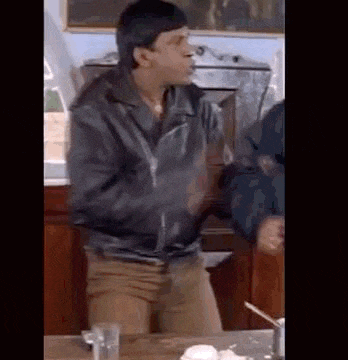 a man in a black leather jacket is standing in front of a table .