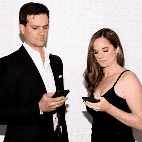 a man and a woman are looking at their cell phones .