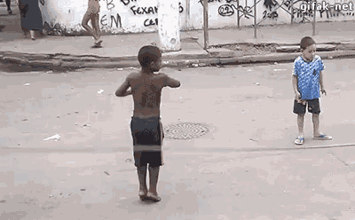 two young boys are playing a game of jumping rope on the street .
