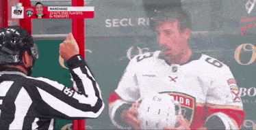 a man in a marchand jersey holds a helmet in front of a referee