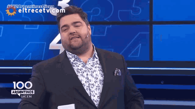 a man in a suit is standing in front of a screen that says 100 argentinas dicen