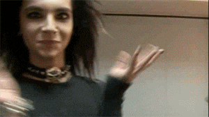 a man with long hair is waving at the camera while wearing a choker .