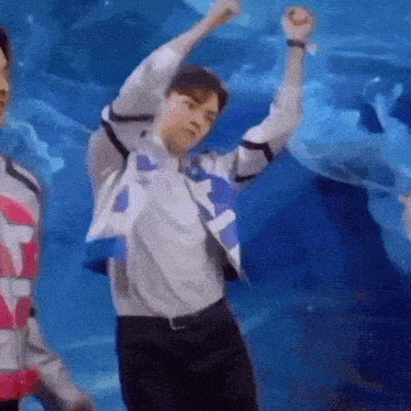 a man is dancing in front of a blue background with his hands in the air .