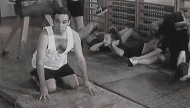 a man in a white tank top is kneeling on a mat