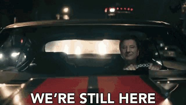 a man in a car with the words we 're still here on the bottom right