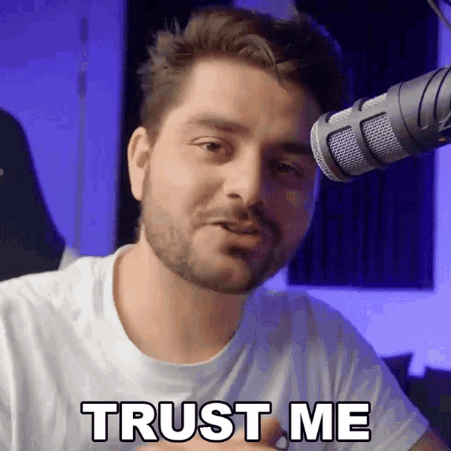 a man with a beard stands in front of a microphone saying " trust me "