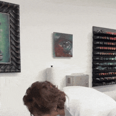 a woman looks down at a painting on a white wall