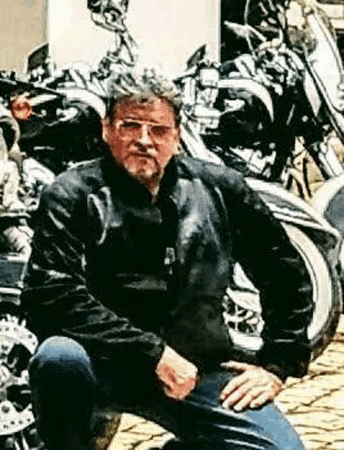 a man is kneeling on a motorcycle in front of a pile of motorcycles .