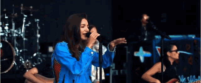 a woman in a blue jacket singing into a microphone on stage