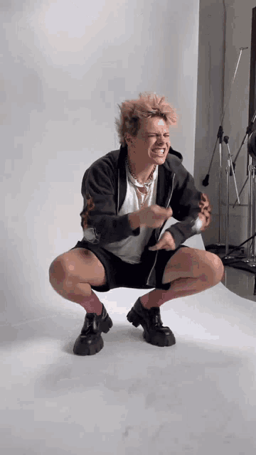 a man with pink hair is squatting down and making a face