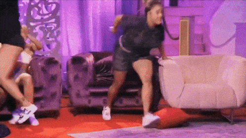 a woman is dancing in a living room while a man sits on a couch