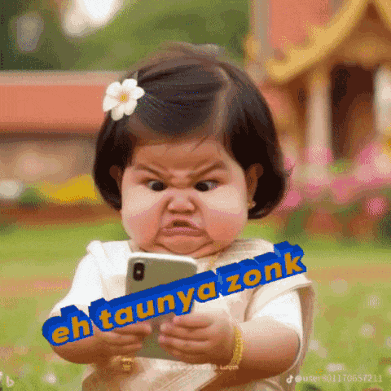a baby with a flower in her hair is holding a cell phone with the words eh taunya zonk written on it