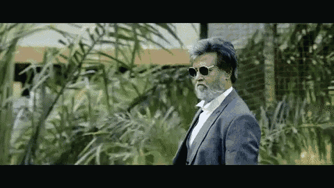 a man with a beard wearing sunglasses and a suit is standing in a forest .
