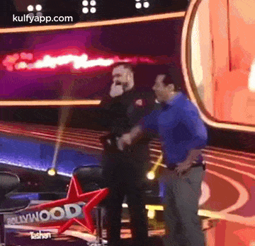 two men are standing next to each other on a stage and one of them is talking into a microphone .