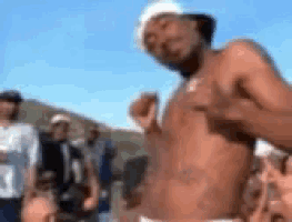 a man without a shirt is standing in front of a crowd of people .