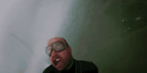 a man wearing goggles and a black shirt is swimming in the water .