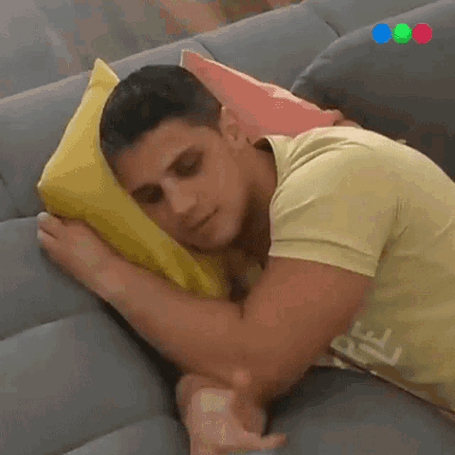 a man is laying on a couch with a yellow pillow and a pink pillow