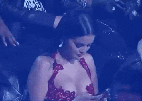 a woman in a red dress is sitting in a dark room looking at her cell phone .