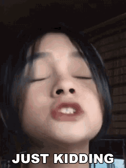 a young girl is making a funny face with her eyes closed and the words `` just kidding '' written on the bottom .
