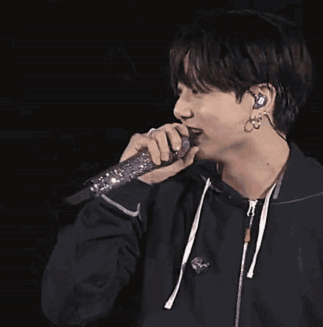 a man wearing a black hoodie is singing into a purple microphone .