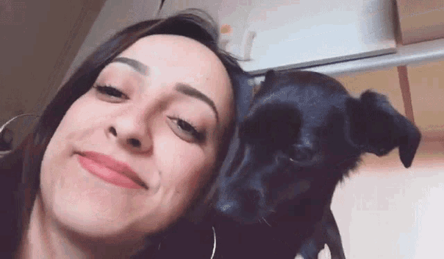 a woman is smiling while holding a black dog on her shoulder .