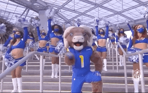 a ram mascot is standing in front of a crowd of cheerleaders wearing face masks .