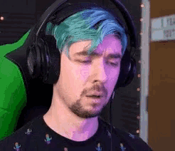 a man with blue hair is wearing headphones and a green chair .