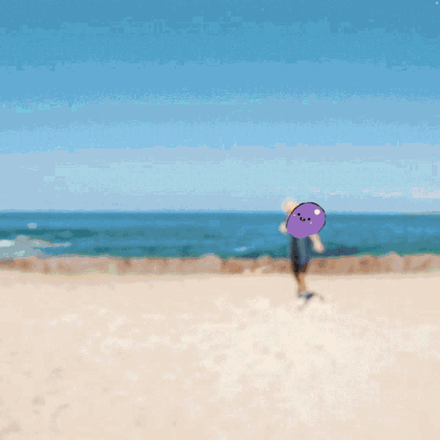 a person playing with a ball on a beach with a purple object on their head