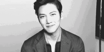 a black and white photo of a young man in a suit and tie making a funny face .