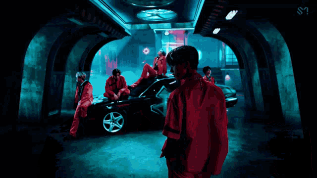 a man in a red jacket is standing in a dark room with a car in the background