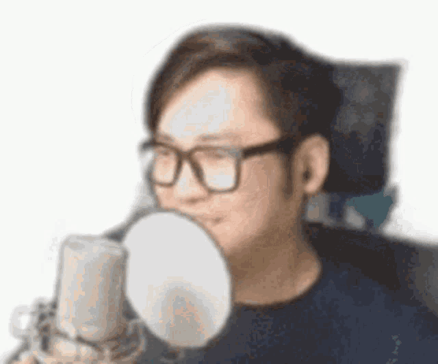 a man wearing glasses is holding a microphone and blowing a bubble .