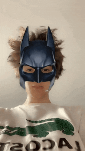 a person wearing a batman mask is wearing a white shirt with a crocodile on it