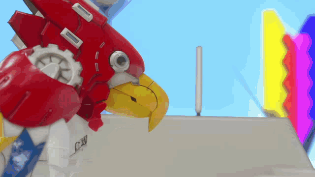 a red robot with a yellow beak is standing in front of a colorful sign that says cw