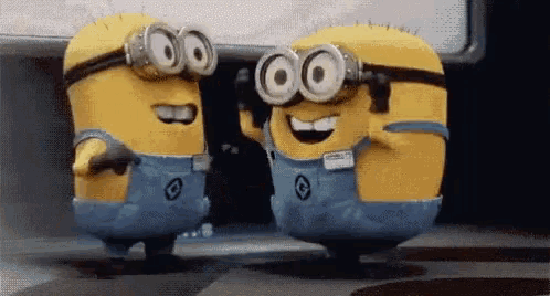 two minions wearing goggles and overalls are standing next to each other and smiling .