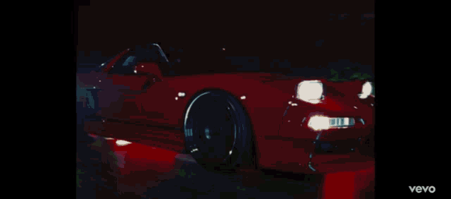 a red car is driving down the street at night through a fence .